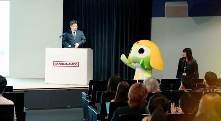 バンダイナムコ未来研究所のホールで行われているライセンシーミーティング。ステージに登壇者が立ち、傍らには着ぐるみのケロロ軍曹が並んでいる様子